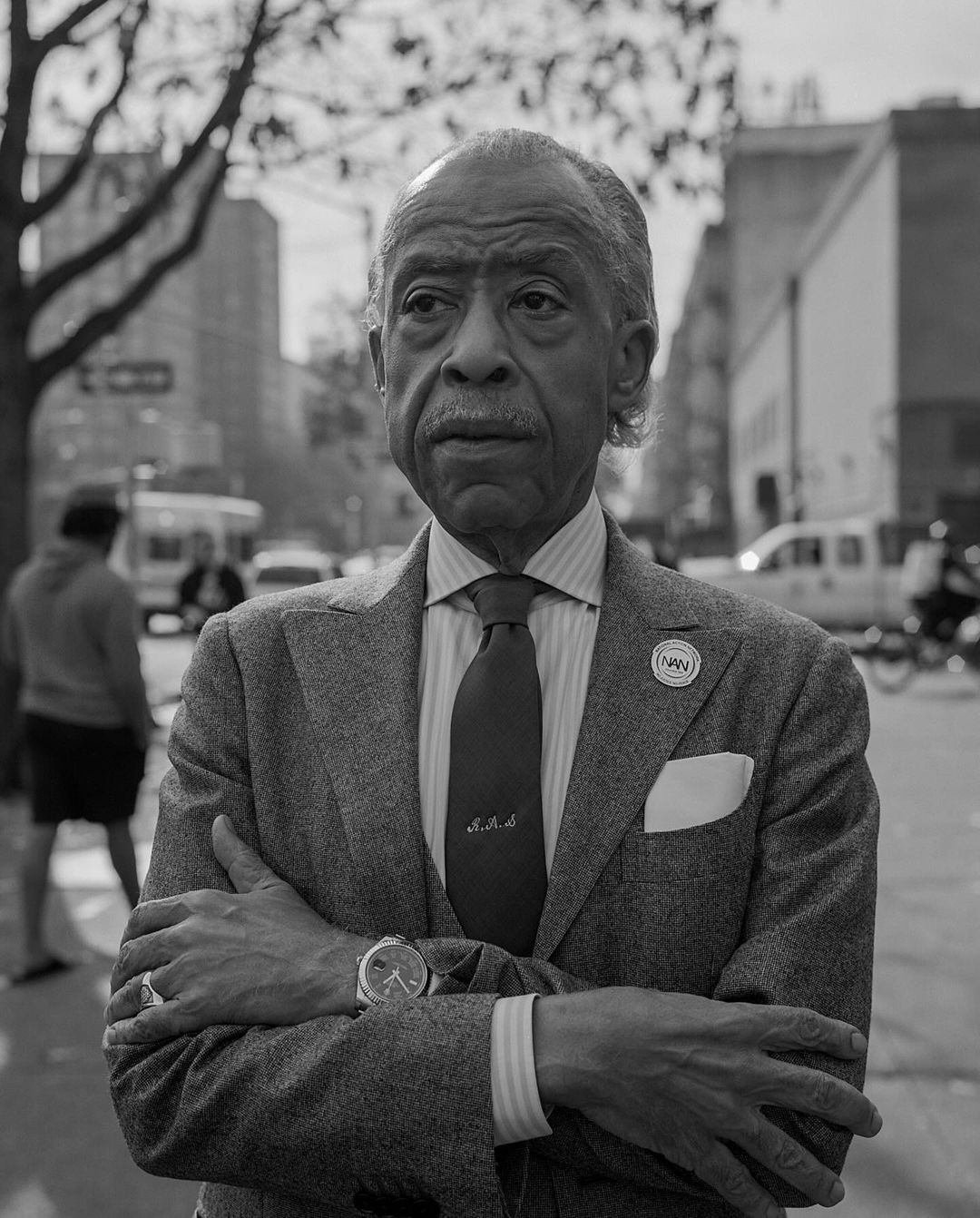 Black and white portrait of Al Sharpton crossing arms wearing a textured suit jacket and tie on a New York street by Andre Wagner.