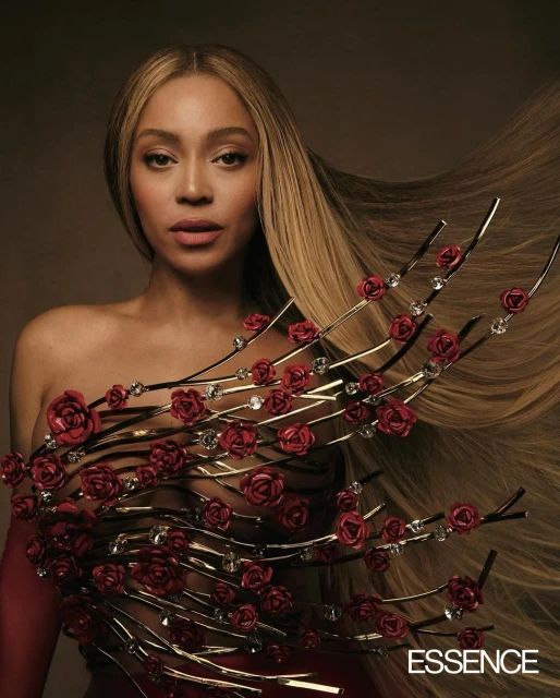 Beyonce poses in a strapless red dress embellished with roses and crystals, showcasing her long blonde hair against a neutral background.