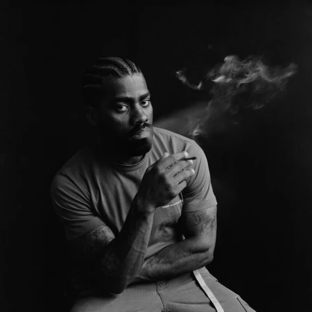 Black man with cornrows and beard smoking a cigarette, captured in a monochrome portrait by photographer Andre Wagner.