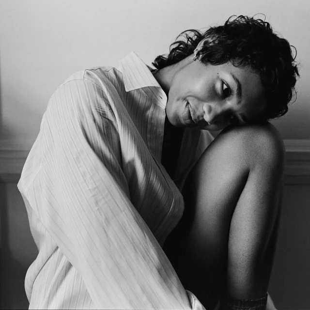 Portrait of a young adult female in a collared shirt, gazing down with a slight smile, captured in black and white with soft lighting.