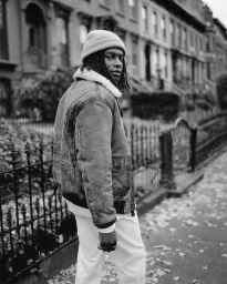 Black man wearing a beanie and shearling jacket on a city street, photographed by Andre Wagner.