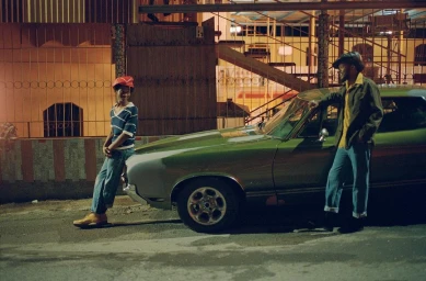 Two men posing next to a vintage green car on a city street at night photographed by Andre Wagner.