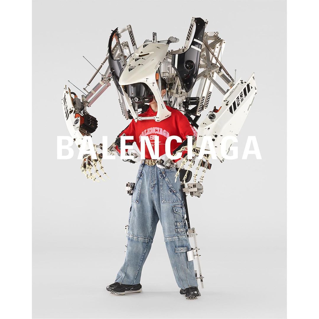 Person wearing a red t-shirt and denim pants with a white and silver mechanical exoskeleton suit against a white background. 