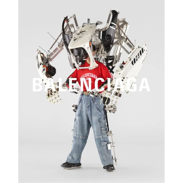 Person wearing a red t-shirt and denim pants with a white and silver mechanical exoskeleton suit against a white background. 