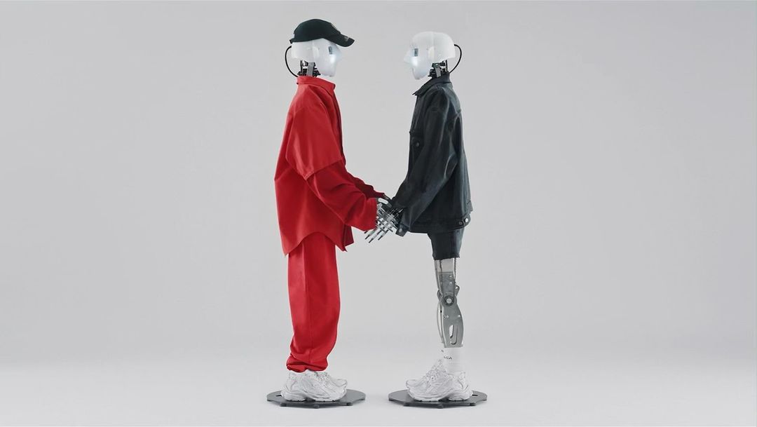 Two robots, one in red and one in black, are standing next to each other and holding hands in a neutral, indoor setting with a white background.