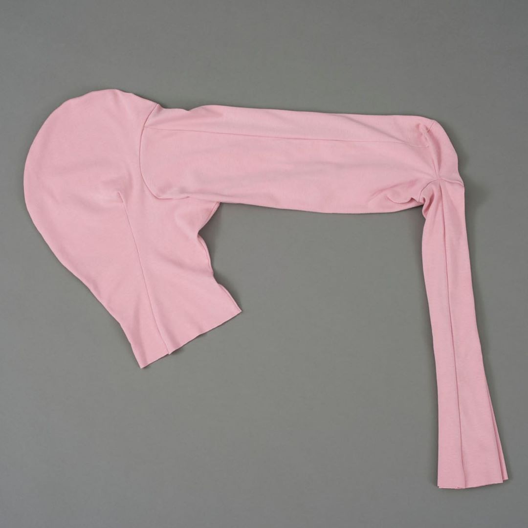 Flat lay of a one-sleeved, pink spandex or nylon garment on a grey background. Fashionable and form-fitting apparel for women.