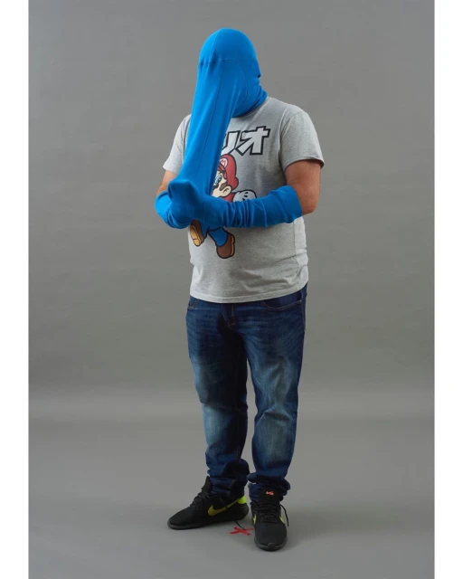Full-length studio shot of a man wearing denim jeans, black sneakers, and a gray t-shirt with a character graphic, covered in a blue fabric.