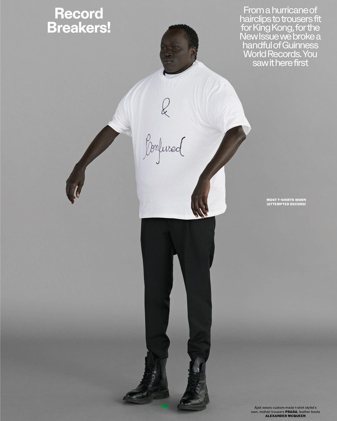 A tall, dark-skinned man stands centered in a full shot, wearing a white '& Confused' t-shirt, black pants, and boots against a neutral backdrop.