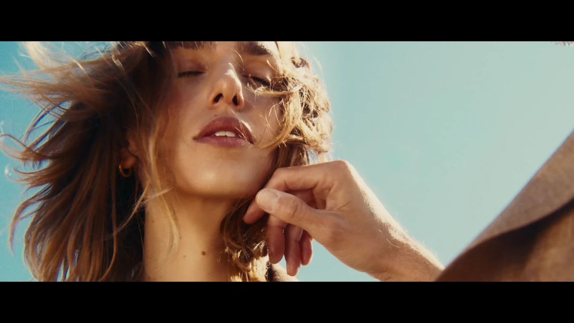 Close-up of a woman with eyes closed and hand near face in warm light, against a clear blue sky backdrop.