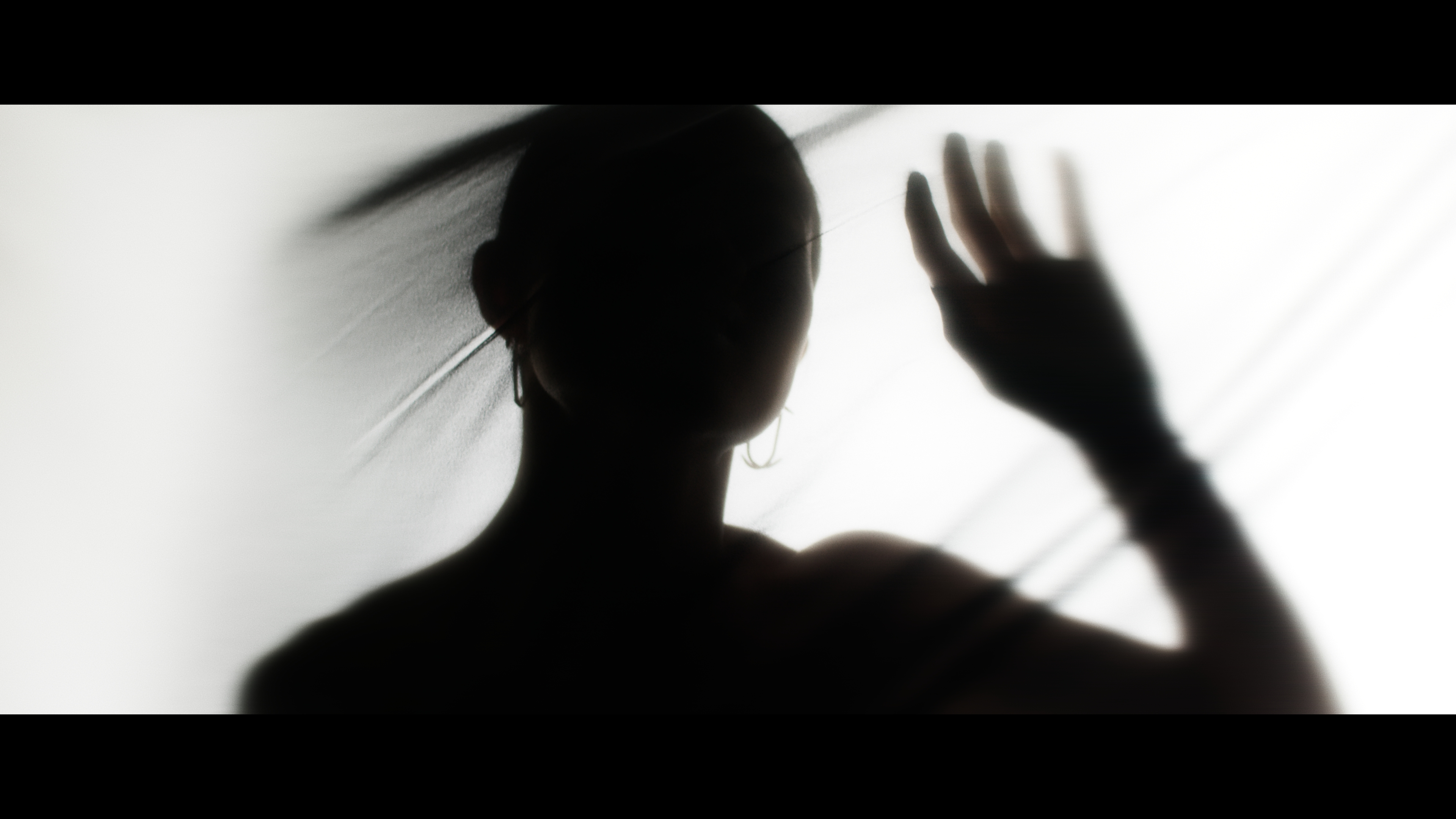 Silhouette of an adult female figure behind translucent fabric, with hand raised, backlit in a softly lit, indoor environment.