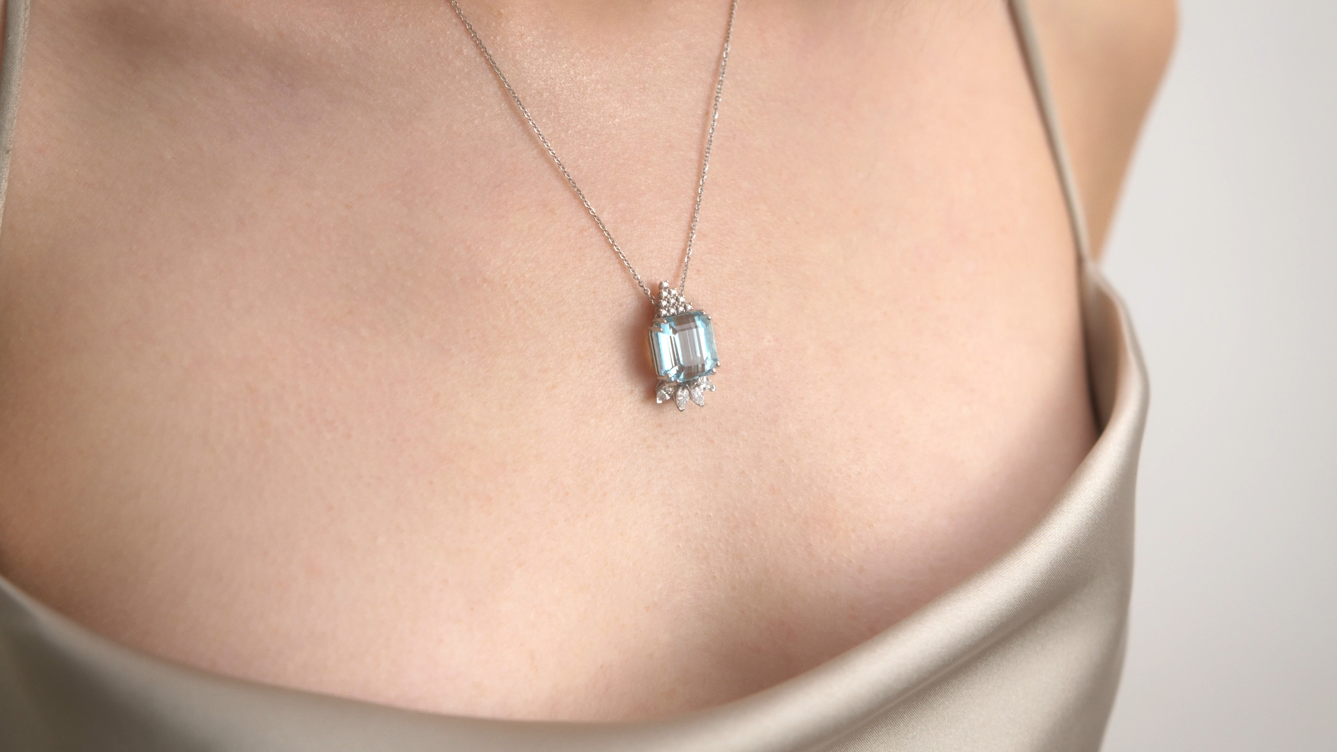Close-up shot of a woman wearing a silver necklace with a blue gemstone pendant, showcasing fashion jewelry against a neutral background.