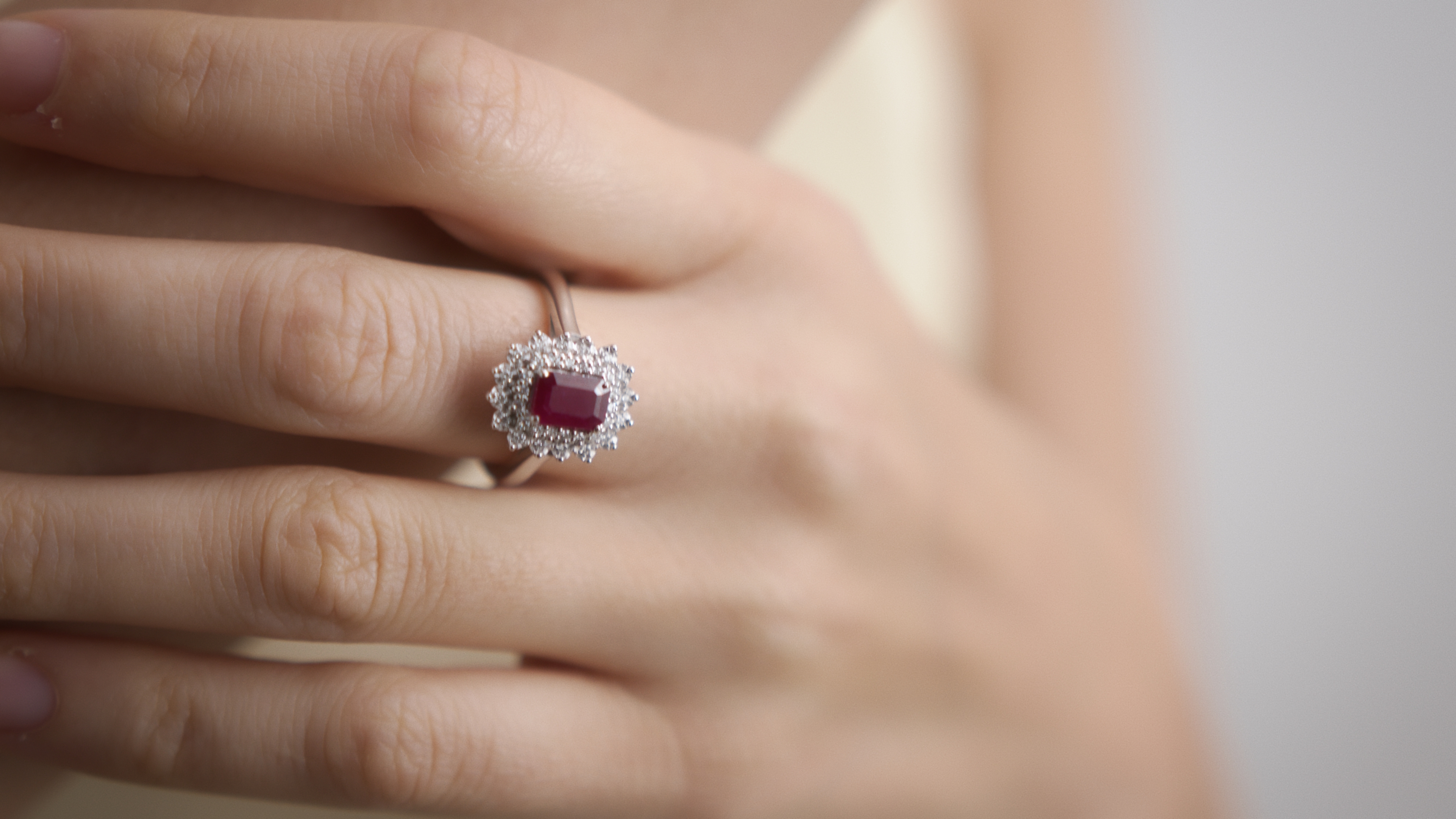Close-up of an adult female hand displaying a silver ring set with a rectangular red ruby surrounded by small clear stones.
