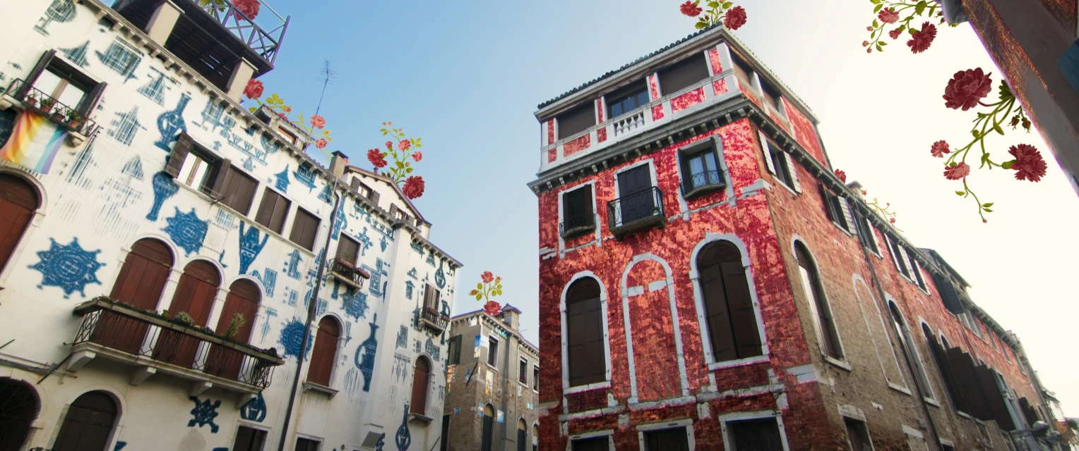Low-angle shot of the exteriors of buildings in Venice with architectural details and red floral illustrations against a bright blue sky.