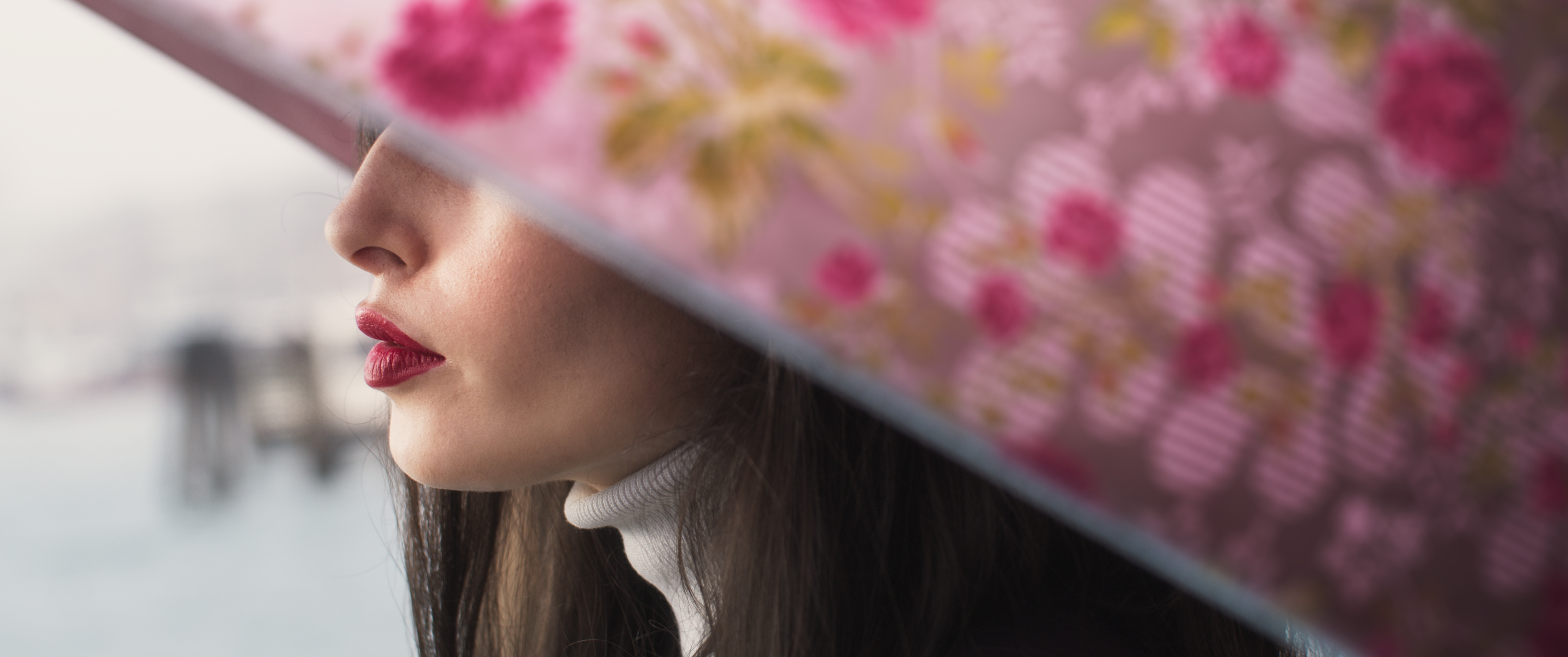 Close-up shot of a woman's face partially obscured by a floral umbrella against an out-of-focus background, showcasing beauty and fashion.