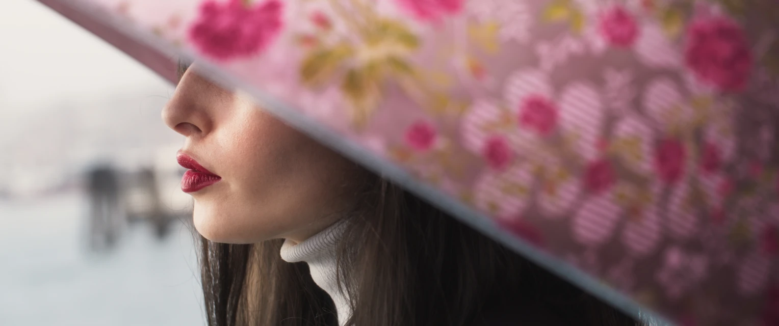 Close-up shot of a woman's face partially obscured by a floral umbrella against an out-of-focus background, showcasing beauty and fashion.