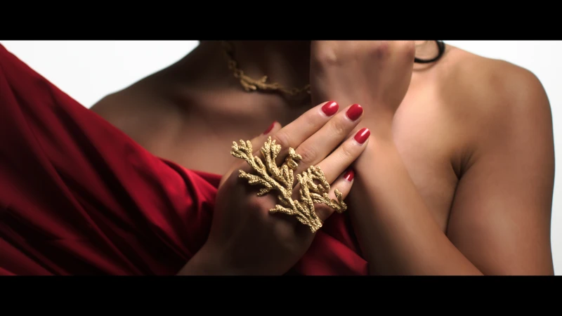 Woman showcases a golden coral ring, complemented by a matching necklace, against a white backdrop, draped in red fabric.