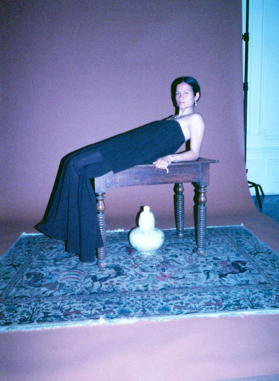 Woman in a black strapless top and trousers lying on a wooden table in a studio with a patterned rug