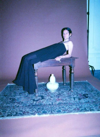 Woman in a black strapless top and trousers lying on a wooden table in a studio with a patterned rug