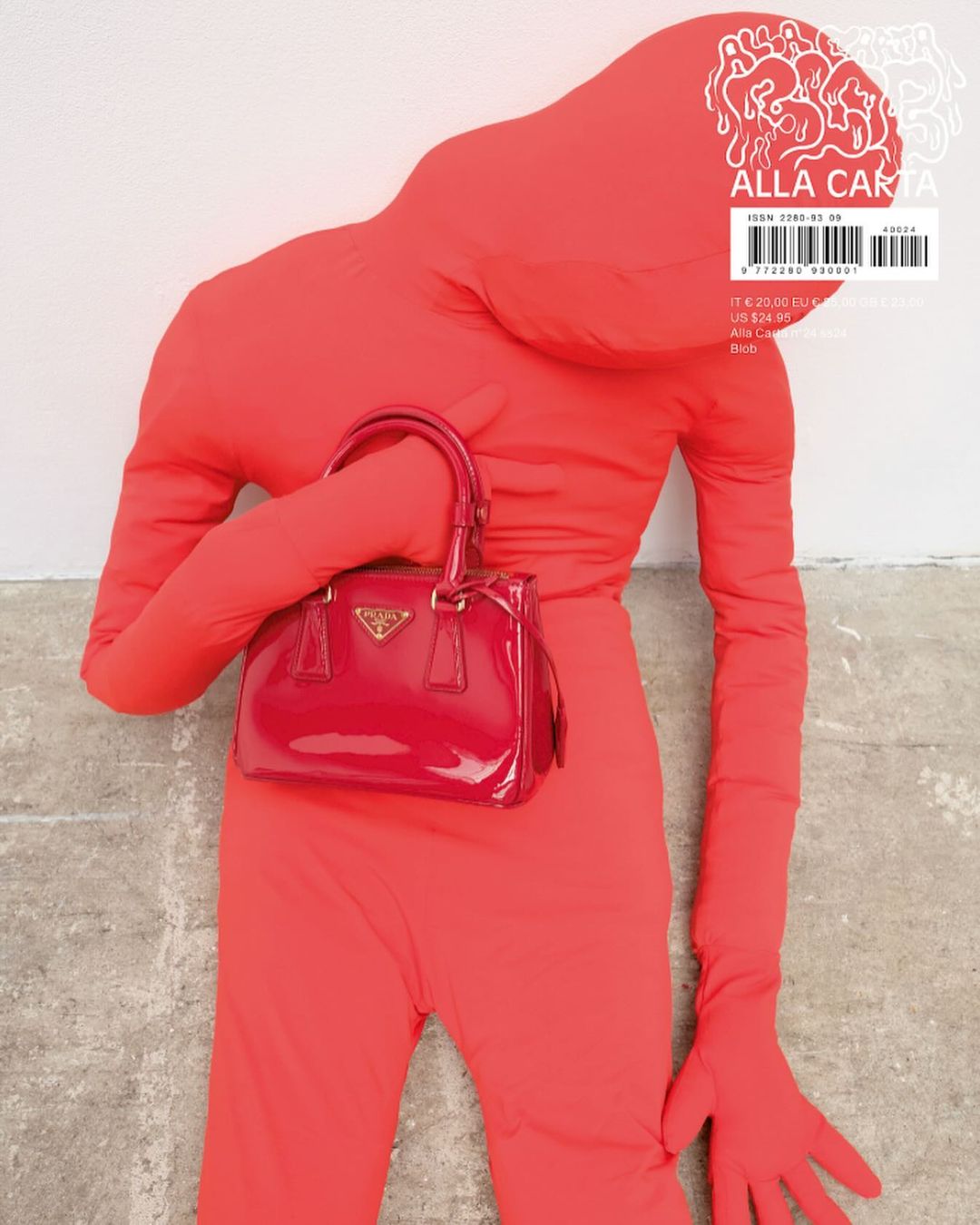 Person in red jumpsuit holds a red Prada purse against a white wall, presented as an editorial fashion statement.