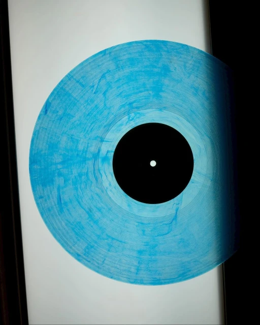 Close-up of a translucent blue marbled vinyl record with a black center on a white surface, partially obscured by a dark shadow.