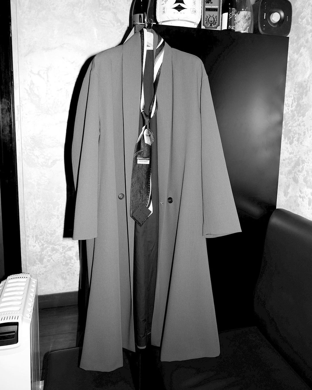 Coat and ties hanging from a garment rack in a monochrome indoor scene. The black and white image features formal attire.
