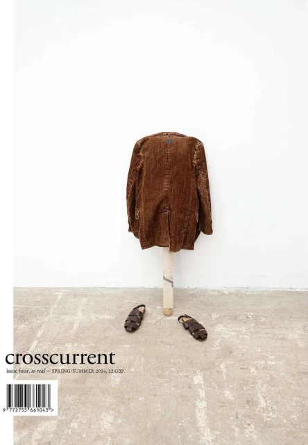 Editorial fashion shot of a brown corduroy jacket hanging on a wooden stand, with a pair of sandals on a concrete floor, magazine cover.