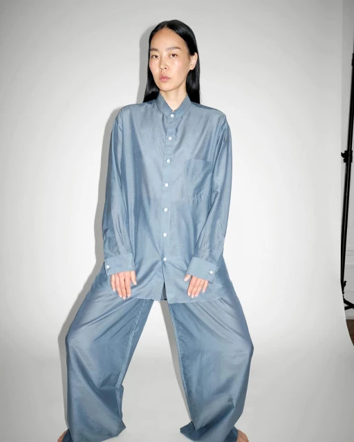 Asian woman in blue oversized shirt and pants in photo studio. She is standing with legs apart looking directly at the camera.