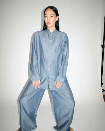 Asian woman in blue oversized shirt and pants in photo studio. She is standing with legs apart looking directly at the camera.