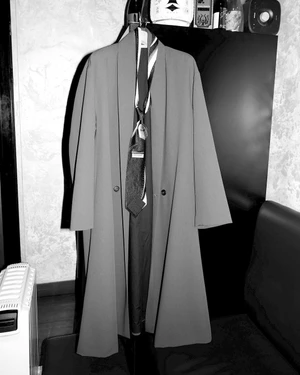 Long coat hanging on a stand with a patterned necktie draped down the front in an interior setting.
