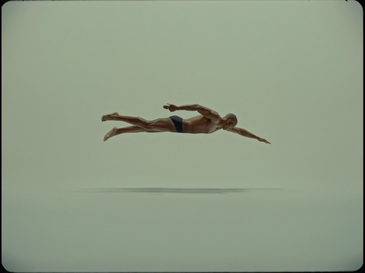 Full shot of a muscular man in a swimming pose against a plain background, showcasing athletic ability, body tone, and dynamic movement.
