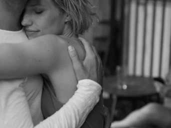 Close-up black and white portrait of a smiling woman embracing a partner, shot by Andreas Baum.