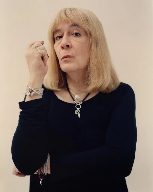 Portrait of an adult female with blonde hair wearing a black long-sleeve shirt and jewelry, posing against a plain white background.