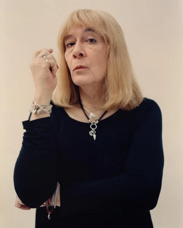 Portrait of an adult female with blonde hair wearing a black long-sleeve shirt and jewelry, posing against a plain white background.