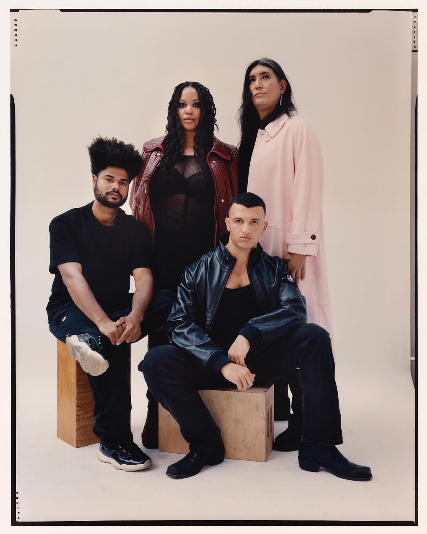 Group portrait of four diverse adults in stylish jackets and outfits posing together in front of a neutral background in a studio setting.
