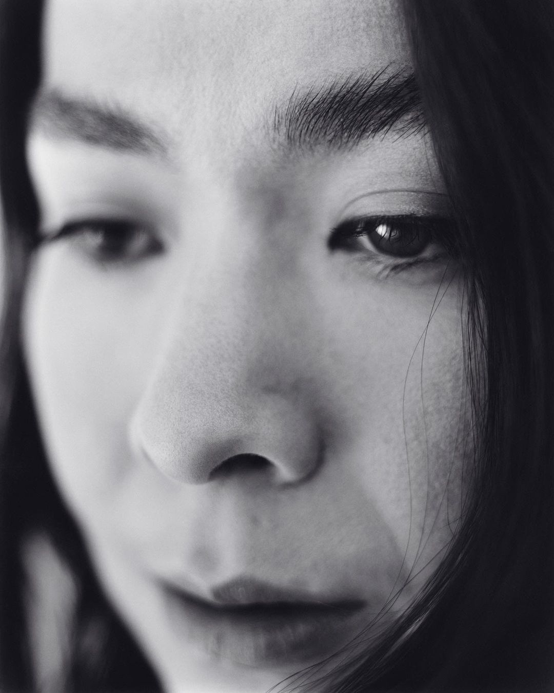 Close-up portrait of an Asian adult female with dark hair looking down. The image is a black and white photograph with soft lighting.