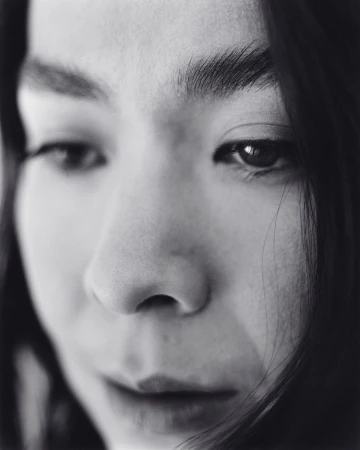 Close-up portrait of an Asian adult female with dark hair looking down. The image is a black and white photograph with soft lighting.