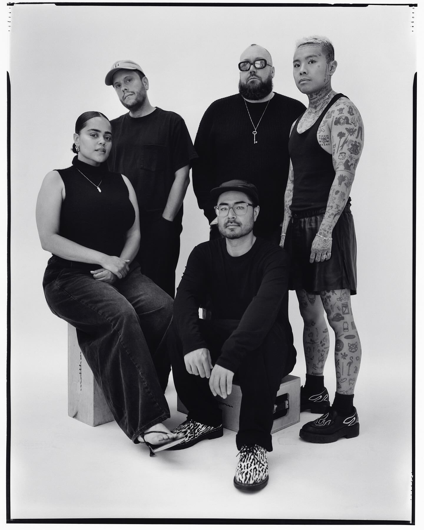 Group portrait of five people in an indoor setting, showcasing a diverse group in a casual yet stylish composition with a white backdrop.