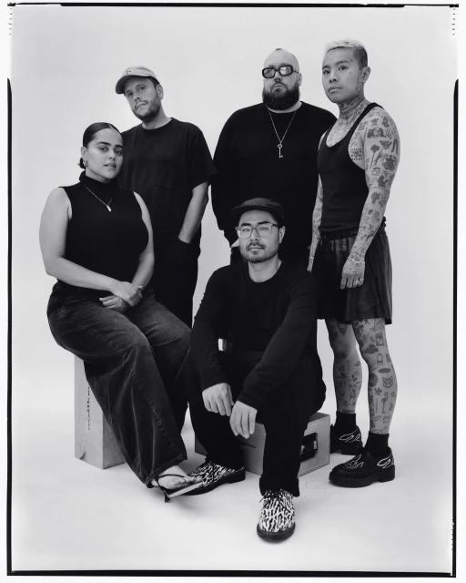 Group portrait of five people in an indoor setting, showcasing a diverse group in a casual yet stylish composition with a white backdrop.