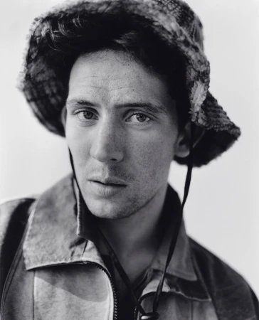 Close-up portrait of a man wearing a bucket hat and jacket against a plain background