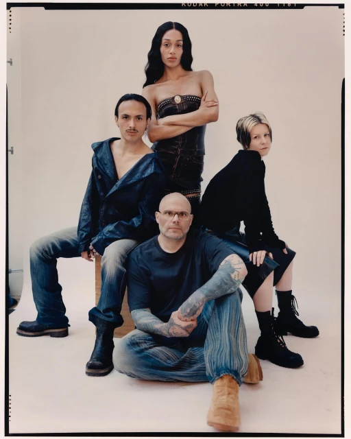 Four people, two adult men and two adult women, seated and standing indoors, in a studio, wearing casual clothing and boots.