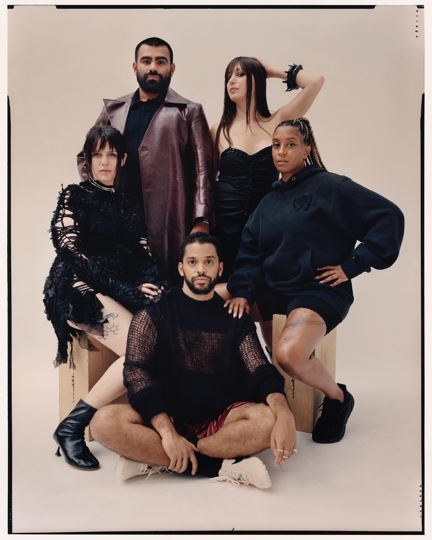 Group portrait of five diverse adults in modern fashion, sitting and standing against a light backdrop in a studio setting.