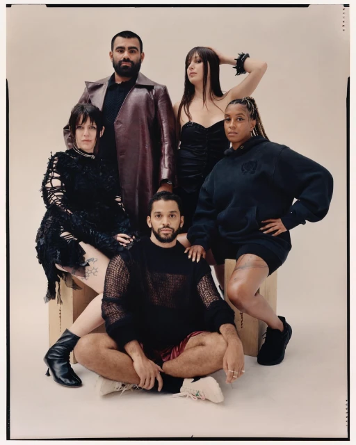 Group portrait of five diverse adults in modern fashion, sitting and standing against a light backdrop in a studio setting.