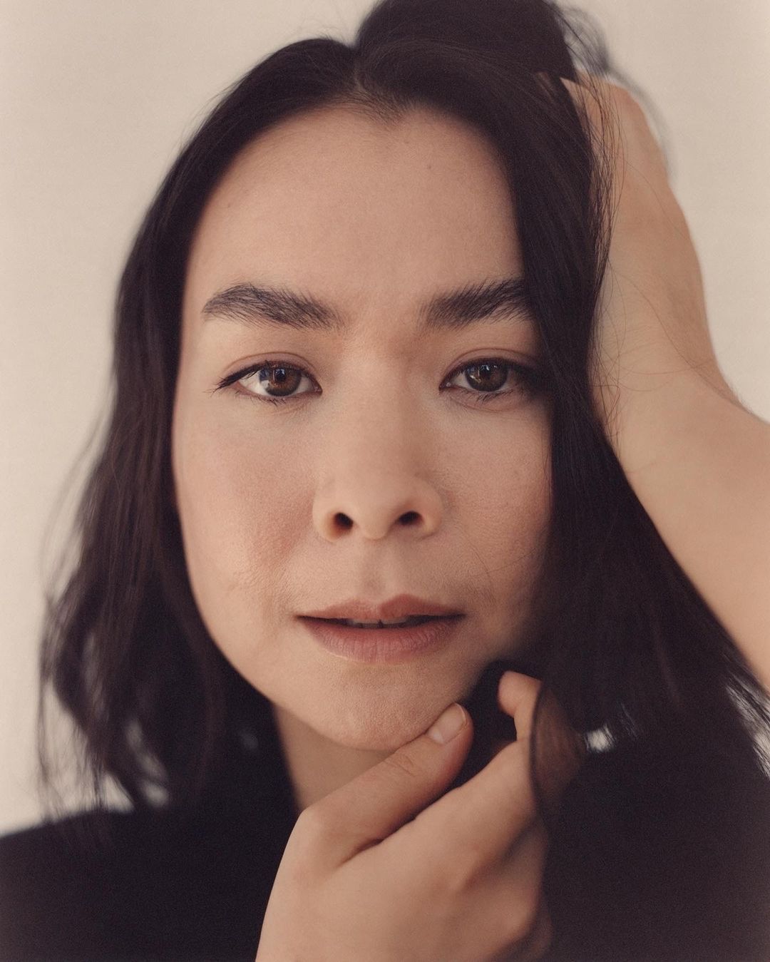 Close-up portrait of a woman with dark hair touching her face, photographed by Andreas Laszlo Konrath.
