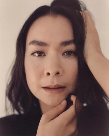 Close-up portrait of a woman with dark hair touching her face, photographed by Andreas Laszlo Konrath.