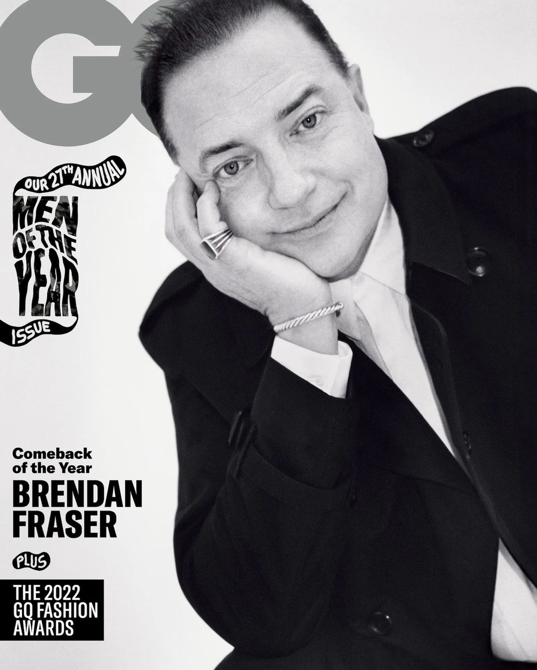 Black and white portrait of Brendan Fraser on the cover of GQ Magazine, wearing a black suit and white shirt. He is resting his face on his hand.