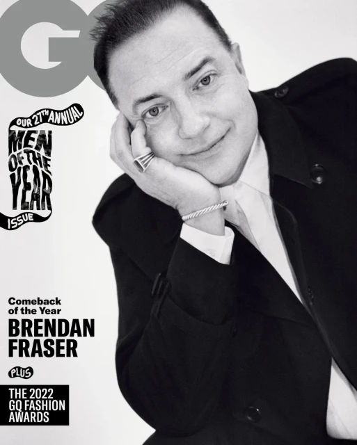 Black and white portrait of Brendan Fraser on the cover of GQ Magazine, wearing a black suit and white shirt. He is resting his face on his hand.