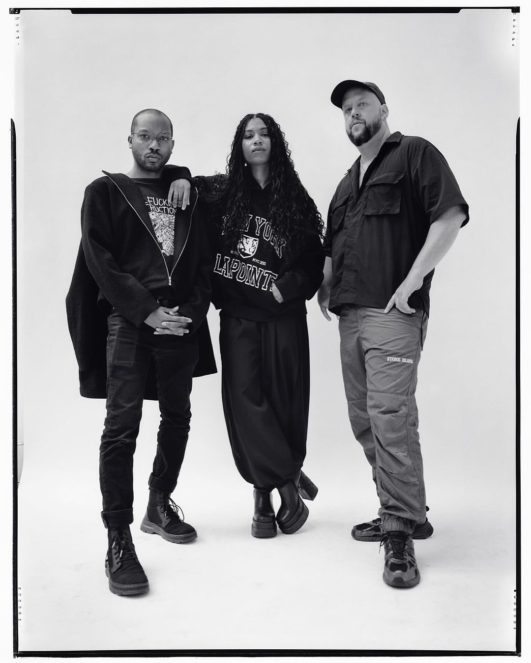 Black-and-white portrait of three people in casual clothes posing in front of a neutral backdrop in a photo studio, full shot.
