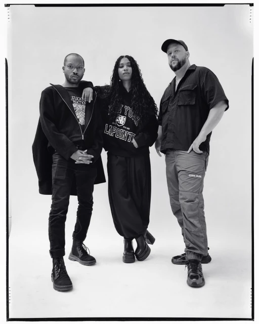 Black-and-white portrait of three people in casual clothes posing in front of a neutral backdrop in a photo studio, full shot.