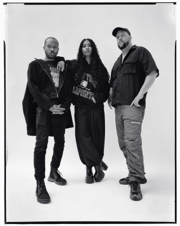 Black-and-white portrait of three people in casual clothes posing in front of a neutral backdrop in a photo studio, full shot.