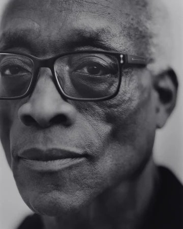 Black and white portrait of an elderly African-American man wearing glasses, looking directly at the camera against a plain background.